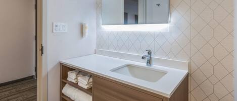 Un baño con lavamanos blanco, tocador de madera y espejo con iluminación integrada.
