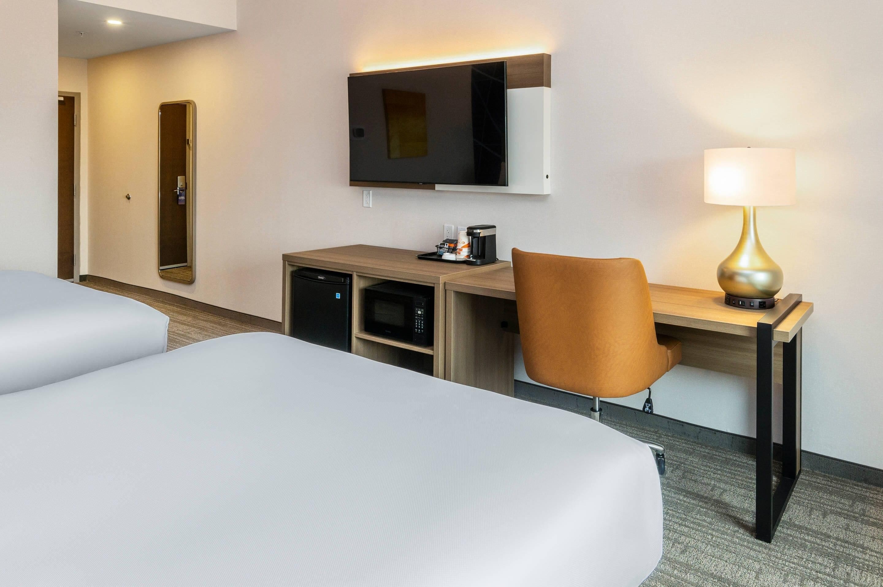 Una habitación de hotel con dos camas, un escritorio con lámpara, televisión y microondas.