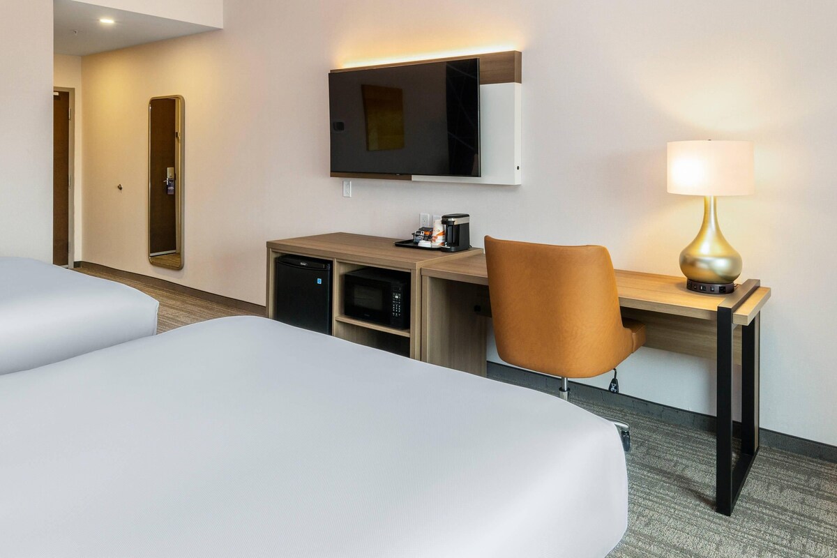 Une chambre d’hôtel avec deux lits, un bureau avec une lampe, une télévision et un four à micro-ondes.