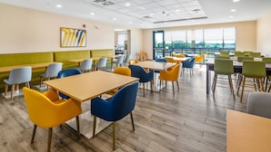 Un espace repas moderne avec des tables et des chaises en bois, un coin salon avec des banquettes vertes et de grandes fenêtres offrant une vue panoramique.