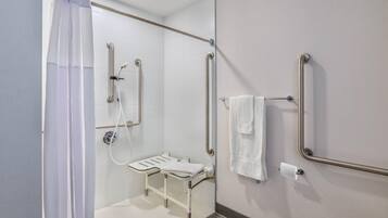 Ein Badezimmer mit Dusche, Haltegriffen, einer rollstuhlgerechten Sitzbank und einem WC mit Haltegriff.