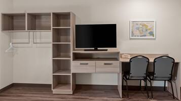 A room with a wooden desk, two chairs, a television, and a wall-mounted shelf unit.