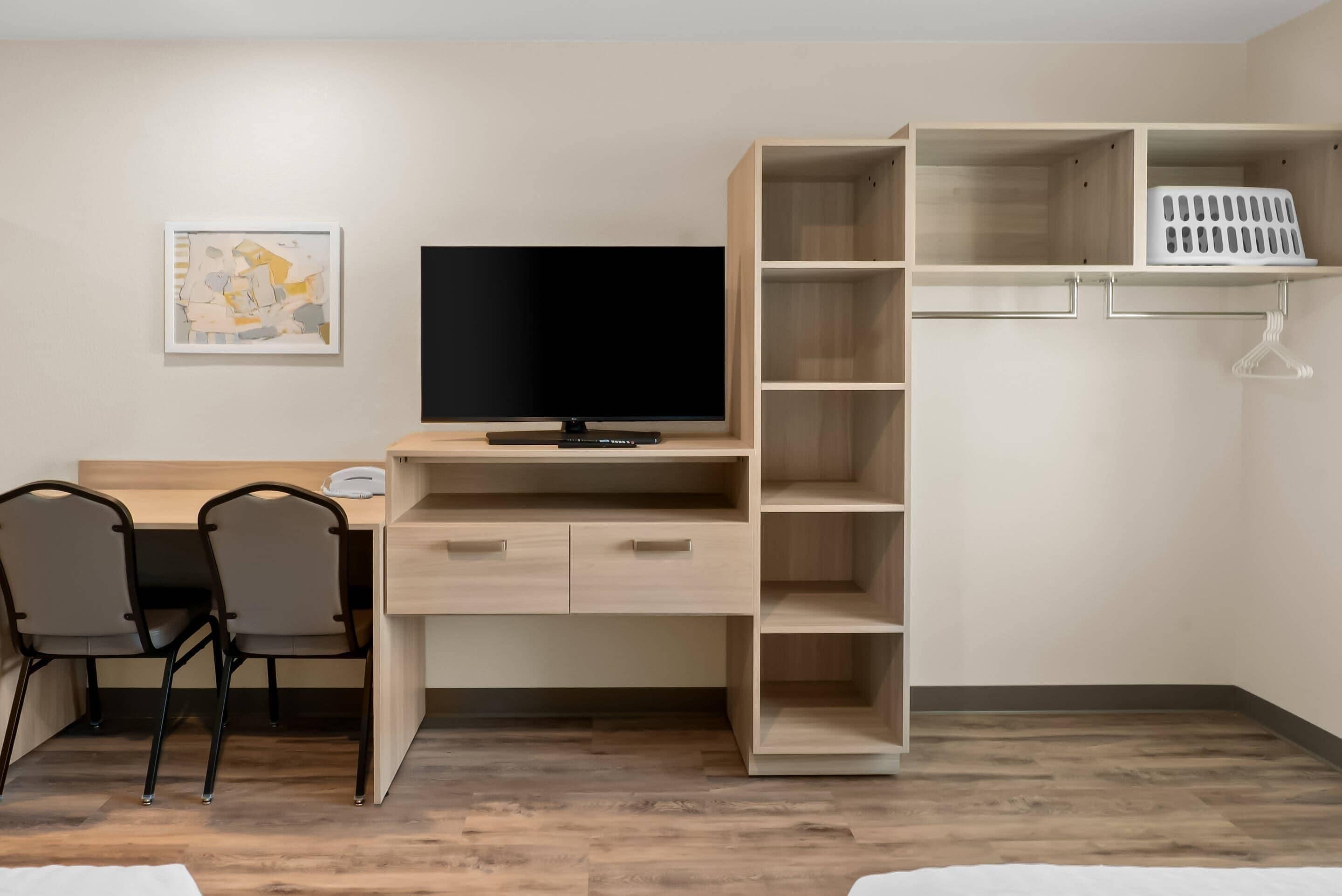 Una habitación moderna con un escritorio de madera, dos sillas, un televisor de pantalla plana y estanterías empotradas.