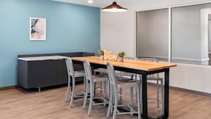 A modern meeting room with a wooden table, grey chairs, a dark grey cabinet, a 'Welcome' sign, and a pendant light. - Woodspring Suites Greenville Airport (Greenville)