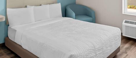 A neatly made bed with white linens in a room with light blue walls and a window.