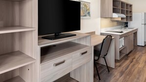 A modern kitchen with wooden cabinetry, a flat-screen TV, and a dining area with a chair. - Woodspring Suites Greenville Airport (Greenville)