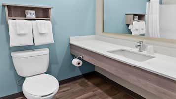 A bathroom with a toilet, a sink, a mirror, and towels on shelves.