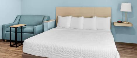 A hotel room with a large bed, a blue armchair, a small table, and a bedside lamp.