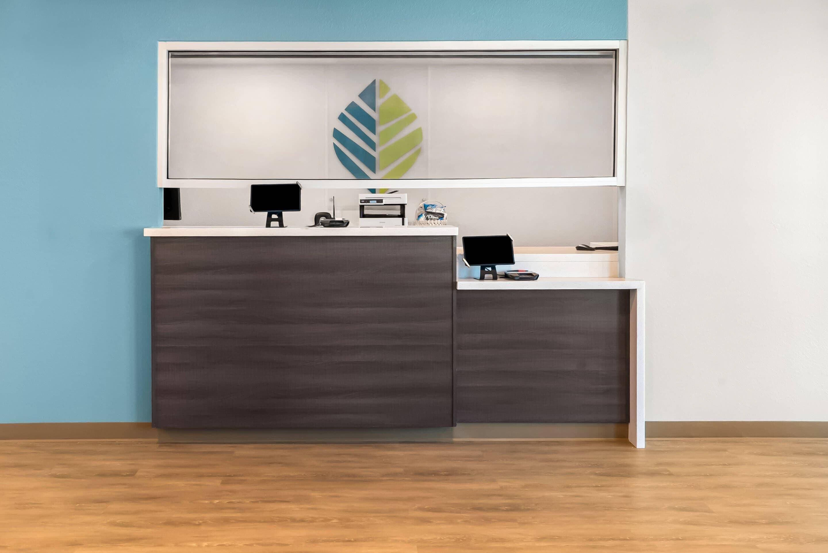 A reception desk with a modern design, featuring a leaf-shaped logo on the wall above.