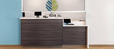 A reception desk with a modern design, featuring a leaf-shaped logo on the wall above.