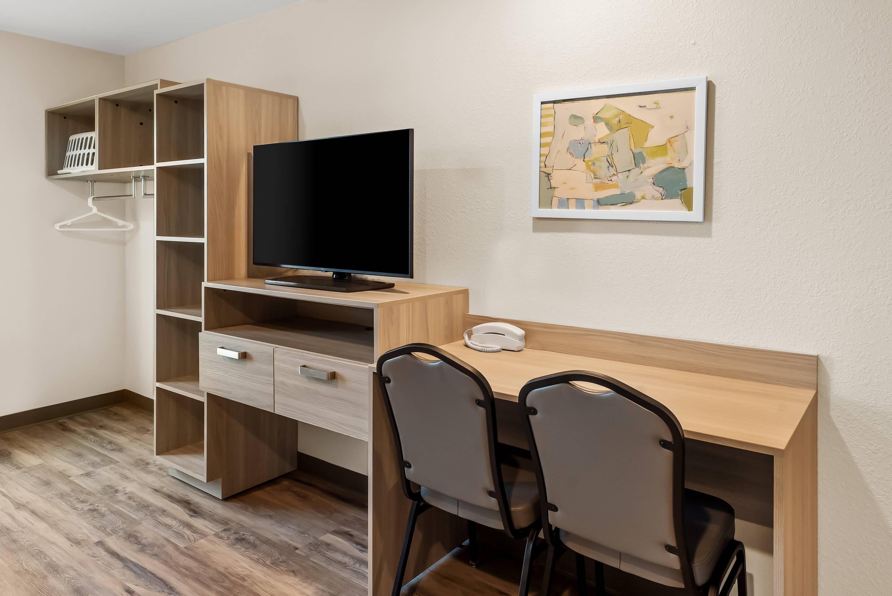 A modern room with a wooden desk, two chairs, a television, and a wall-mounted art piece.