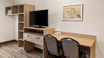 A modern room with a wooden desk, two chairs, a television, and a wall-mounted art piece.