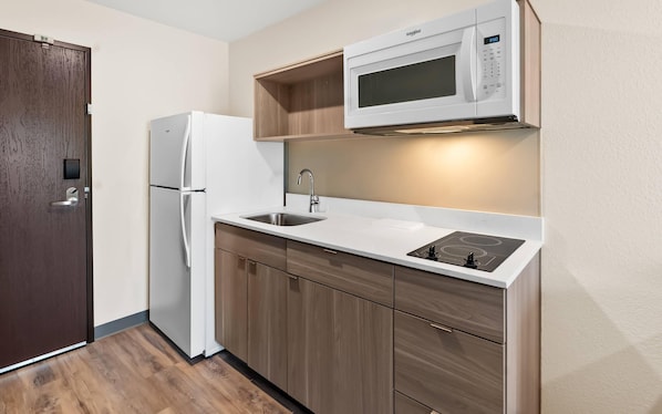 Una cocina compacta con un refrigerador blanco, un microondas, un lavamanos y armarios de madera.