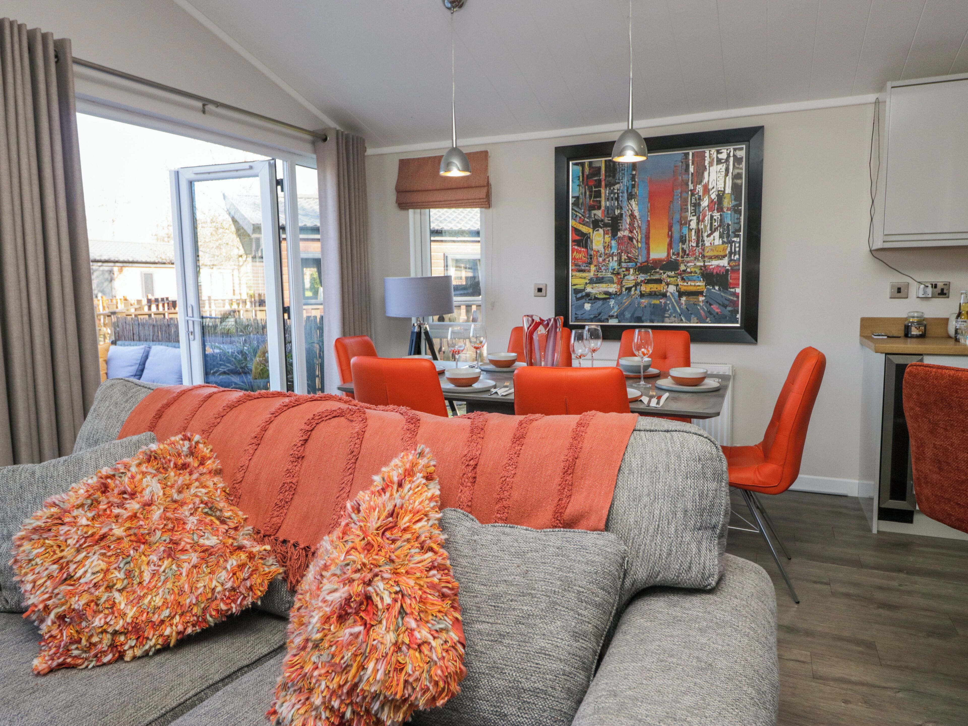 A modern living room with a grey sofa, orange cushions, a dining area with orange chairs, and a cityscape painting on the wall.
