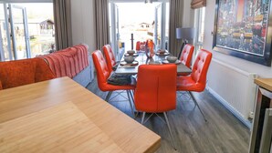 A dining area with a long wooden table, red chairs, and a view of the outside through large windows. - Coniston View Lodge (Carnforth)