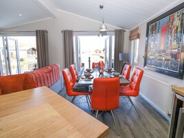 Uma sala de jantar com uma mesa de madeira comprida, cadeiras vermelhas e vista para o exterior através de janelas grandes.