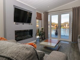 Uma sala de estar moderna com lareira, televisão de tela plana e vista para um lago através de grandes portas de vidro.