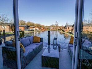 Un'area salotto esterna moderna con una barriera in vetro, un canale d'acqua e edifici in legno sullo sfondo.
