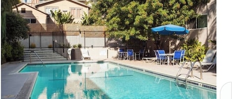 Piscina com água azul cristalina, rodeada por espreguiçadeiras e um guarda-sol azul.