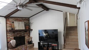 Ein Wohnzimmer mit Kamin aus Backstein, Flachbildfernseher, Deckenventilator und einer Treppe.