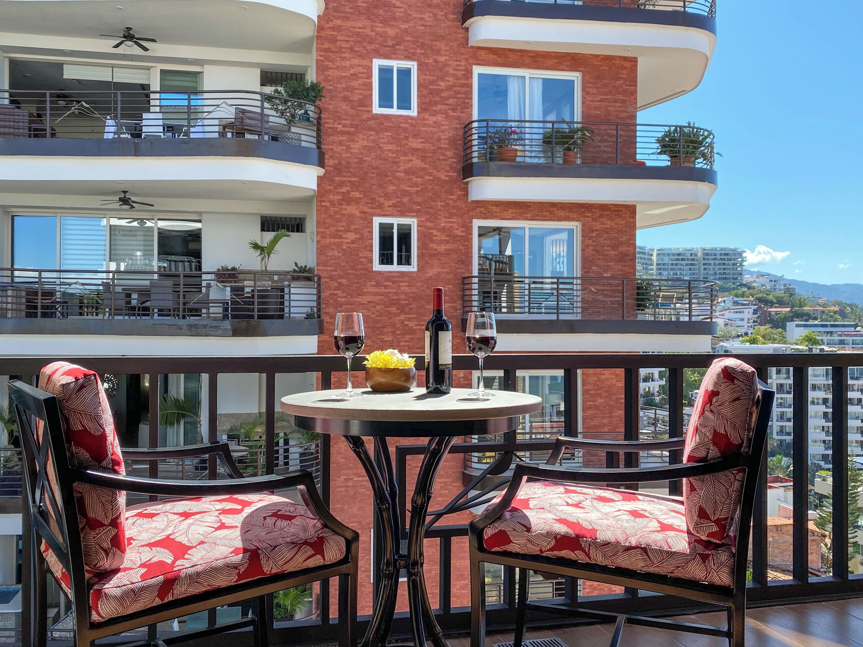 A balcony with two chairs, a table, and a bottle of wine.