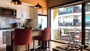 Une cuisine moderne équipée d’un four à micro-ondes, d’une cuisinière et de tabourets de bar. Un balcon avec des sièges d’extérieur est visible à travers une grande fenêtre.