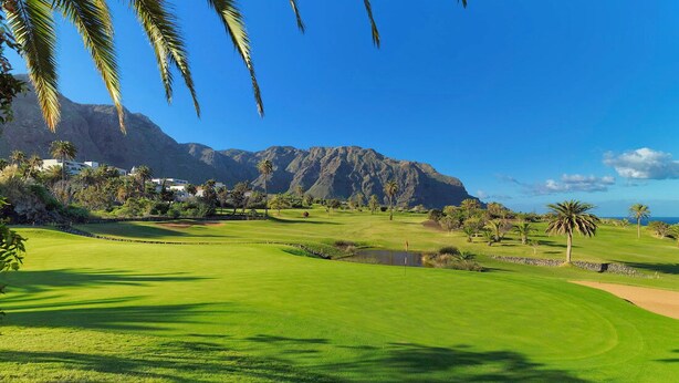 Ein Golfplatz mit Bergblick, Palmen und blauem Himmel.