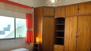 Ein Schlafzimmer mit zwei Betten, einem Holzschrank, einem Nachttisch mit Lampe und einem Fenster mit Vorhängen.