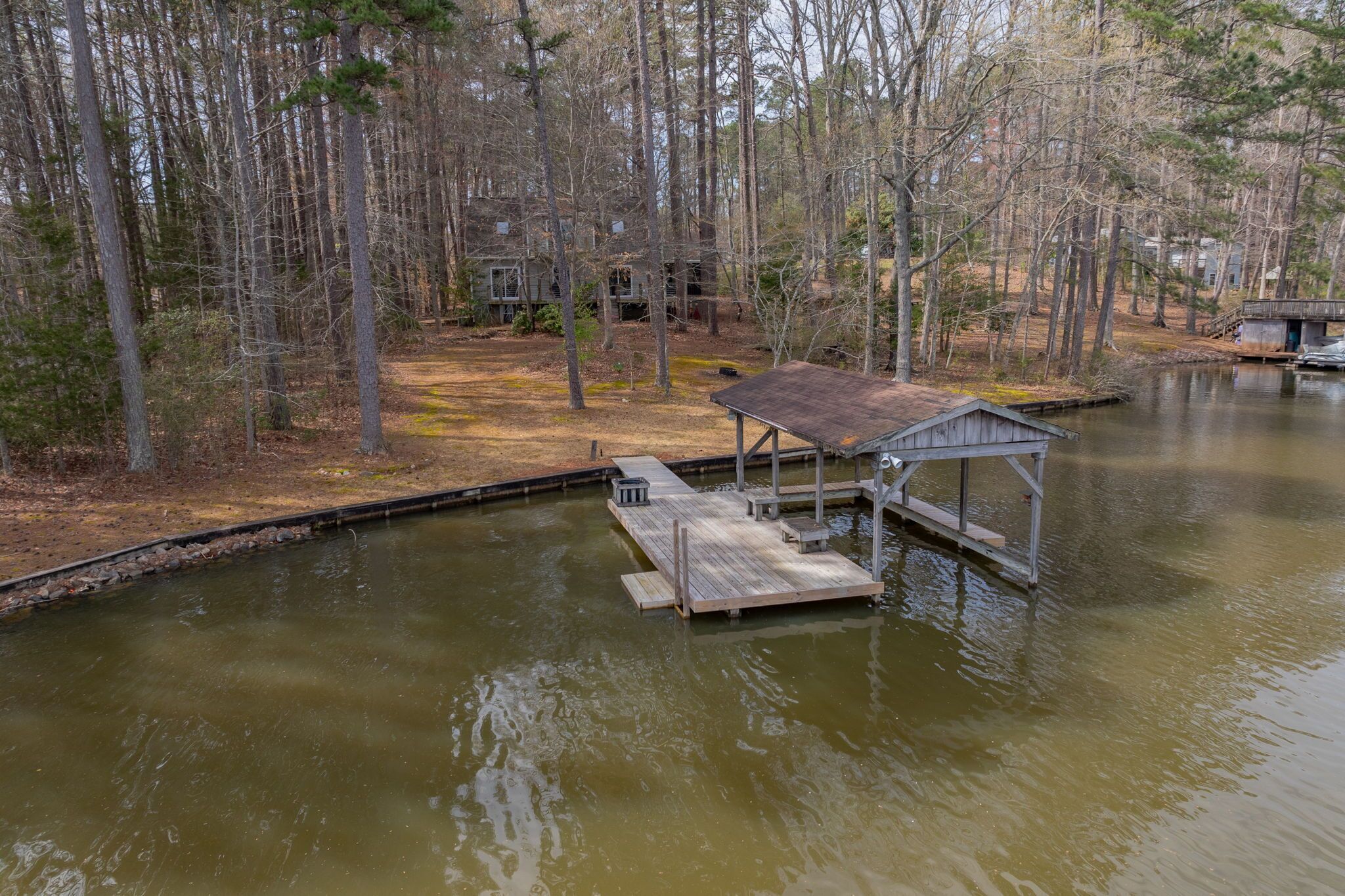 A wooden dock extending into a calm lake, surrounded by trees and a small cabin.