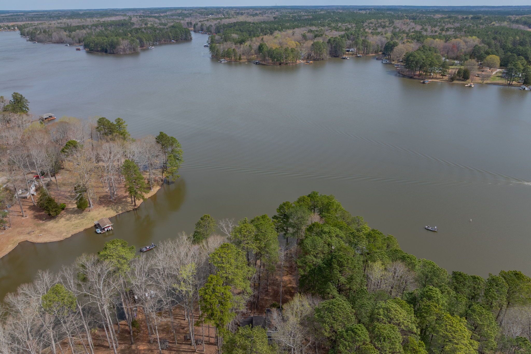 An aerial view of a river with boats, surrounded by dense forest and some buildings.