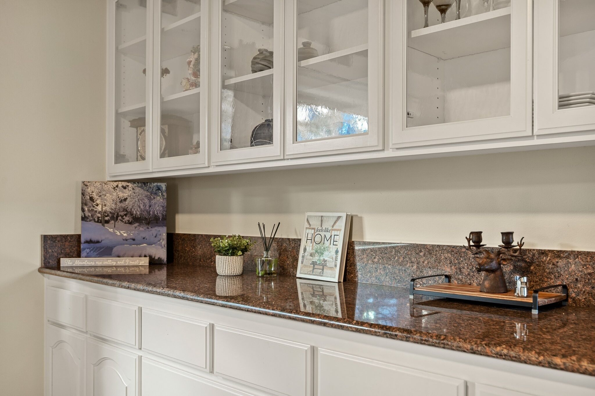 A kitchen with white cabinets, a granite countertop, and a glass-fronted cabinet above.