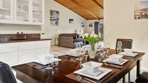 Un comedor con una mesa de madera dispuesta para cuatro, armarios blancos y vistas a una sala de estar al fondo.