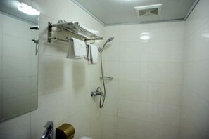 Ein Badezimmer mit weißen Fliesen, einer Dusche, einem Handtuchhalter und einer Toilette.