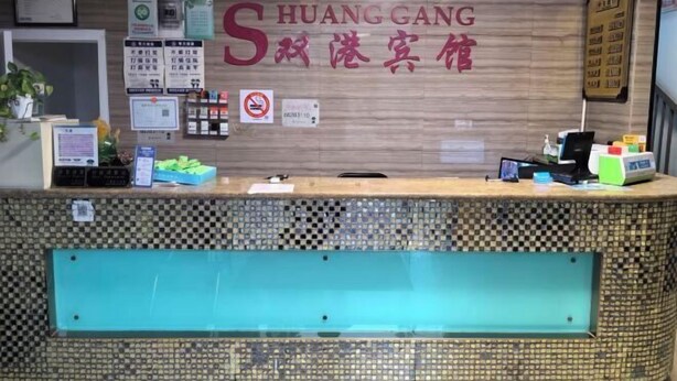 A hotel reception desk with a check-in counter, a wall-mounted sign with the hotel's name, and various informational posters and notices. - Shuanggang Hotel (Shanghai)