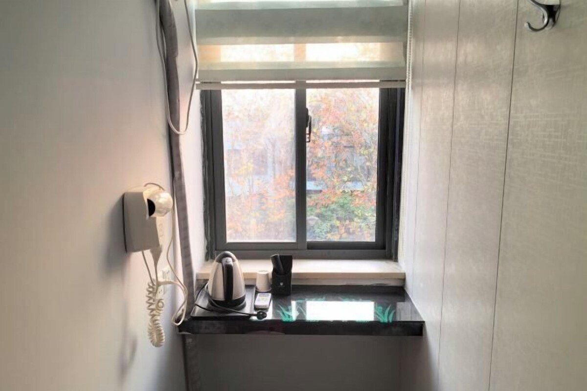 Una pequeña kitchenette con ventana, teléfono y hervidor sobre la encimera.