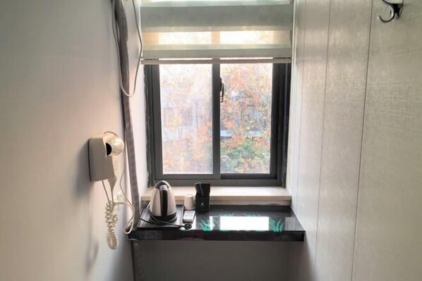 Una pequeña kitchenette con ventana, teléfono y hervidor sobre la encimera.