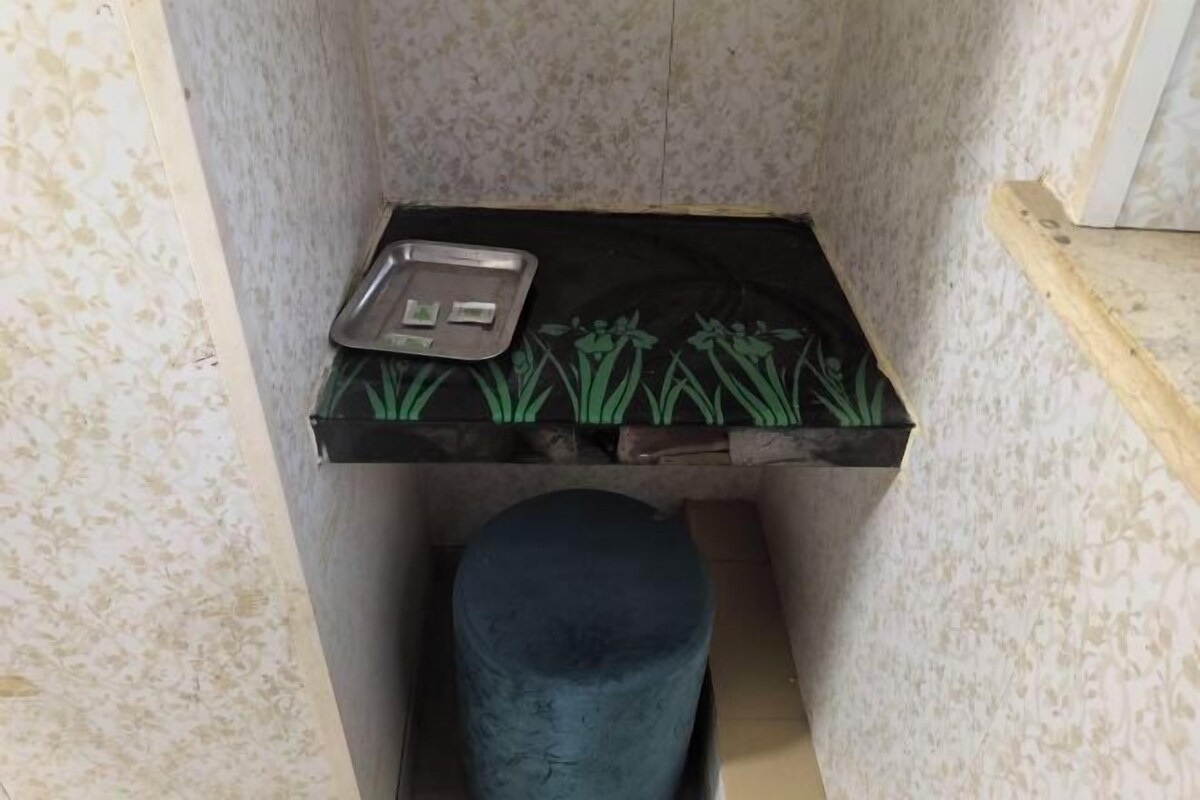 Espacio pequeño y cerrado con una pared decorada, una bandeja metálica con un objeto pequeño sobre una superficie negra, y un taburete oscuro.