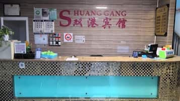 Una reception hotel con un banco accettazione, una targa appesa al muro con il nome dell'hotel, un cartello che vieta di fumare e diversi manifesti informativi.