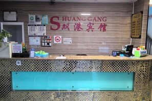 A hotel reception desk with a check-in counter, a wall-mounted sign with hotel name, a no-smoking sign, and various informational posters. - Shuanggang Hotel (Shanghai)
