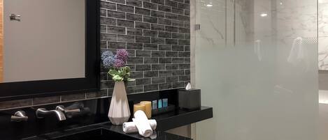 A modern bathroom with a black countertop, a mirror, a vase with flowers, and a glass shower enclosure.