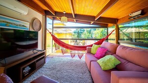 Un salon avec un plafond en bois, un téléviseur à écran plat, un hamac rouge et un canapé agrémenté de coussins colorés.