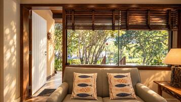 Quarto com sofá, janela com persianas, luminária e vista para árvores.