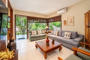 A spacious living room with a sofa, a coffee table, and a view of greenery outside. - Bz21 Casa com Jacuzzi e churrasqueira (Buzios)