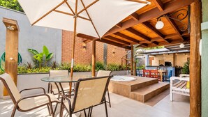 An outdoor patio area with a glass table, chairs, a wooden bench, and a large umbrella. - Bz21 Casa com Jacuzzi e churrasqueira (Buzios)