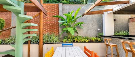 Eine Terrasse mit Holztisch und -stühlen, umgeben von Pflanzen und einer Backsteinmauer.