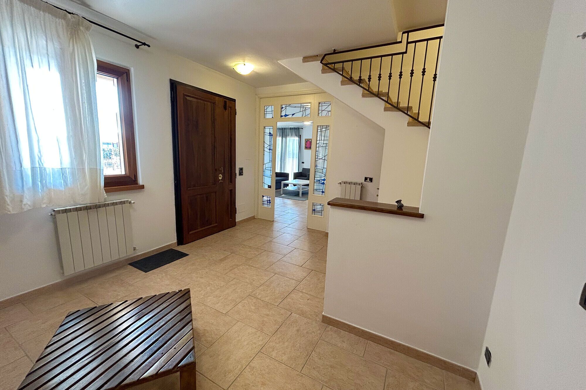 A hallway with a wooden bench, a radiator, a door, and a staircase.