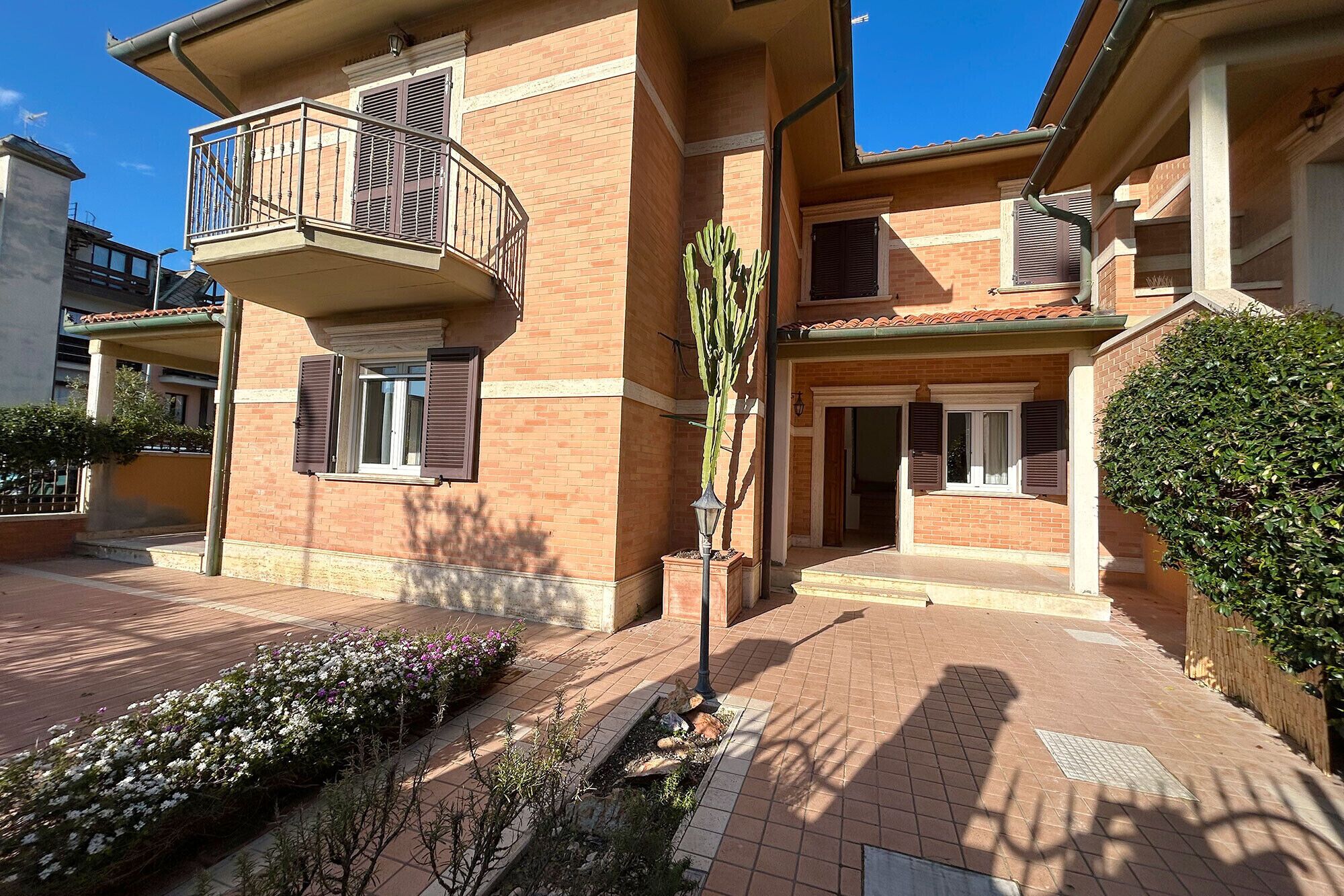 A multi-story residential building with a balcony, a small garden area with flowers, and a well-maintained exterior.