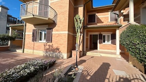 A multi-story residential building with a balcony, a small garden area with flowers, and a well-maintained exterior.