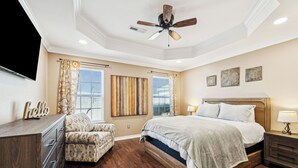 A bedroom with a large bed, a ceiling fan, a dresser, a chair, and artwork on the walls. - Spin and Stay on Navajo (Bentonville)