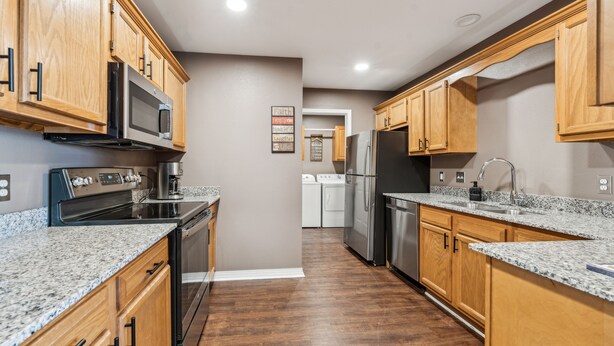 A modern kitchen with wooden cabinets, granite countertops, stainless steel appliances, and a central island. - Spin and Stay on Navajo (Bentonville)